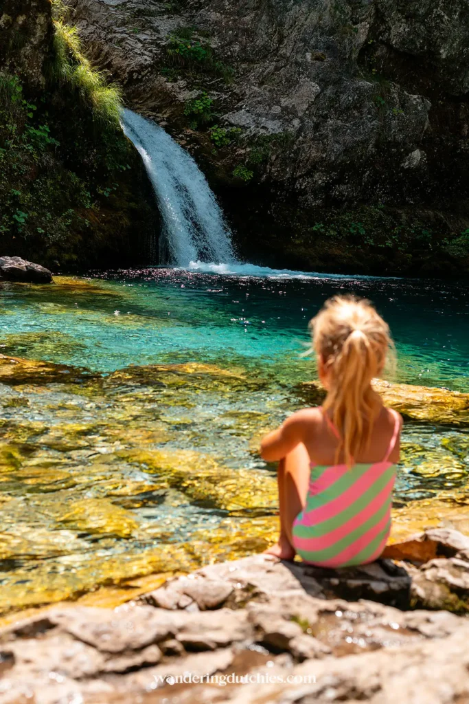 Child looking at the Blue Eye in Theth, Albania, a crystal-clear natural pool with a waterfall.