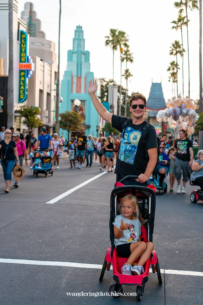 Vader met dochter in een buggy poseert op Hollywood Boulevard in Disney’s Hollywood Studios, omringd door de klassieke art-decostijl gebouwen.