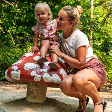 Marissa en Nina zitten bij een kleurrijke paddenstoel in het Sprookjesbos van de Efteling, genietend van de sprookjesachtige sfeer.