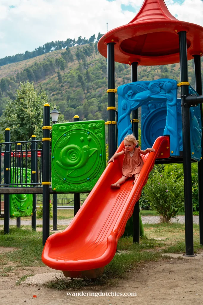 Kind glijdt van de rode glijbaan in een speeltuin langs de boulevard in Berat, Albanië.