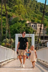 Vader en dochter wandelen over een brug met uitzicht op de groene heuvels en stenen gebouwen van Berat, Albanië.