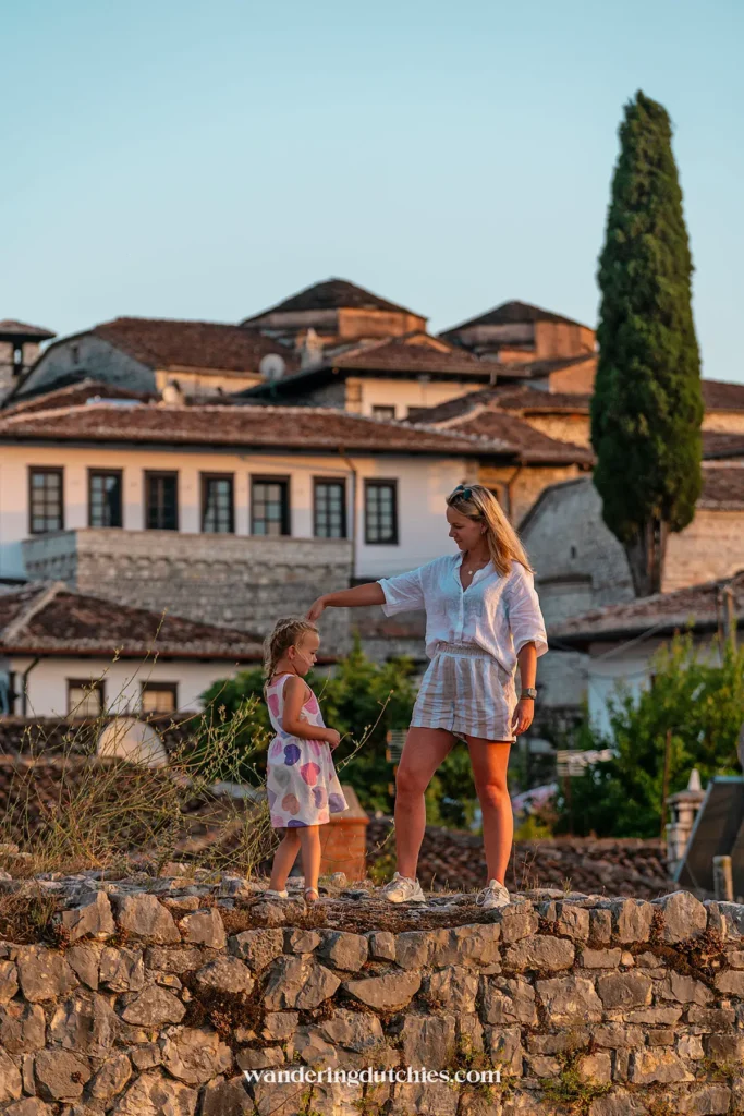 A mother and daughter dancing on the castle walls of Berat Castle at sunset, with traditional Albanian buildings in the background.