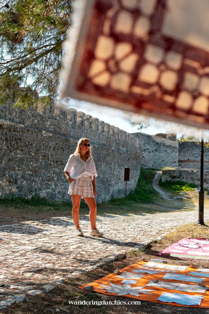 Kleurrijke stoffen en handgemaakte producten worden tentoongesteld in Berat Castle, met stenen muren op de achtergrond.