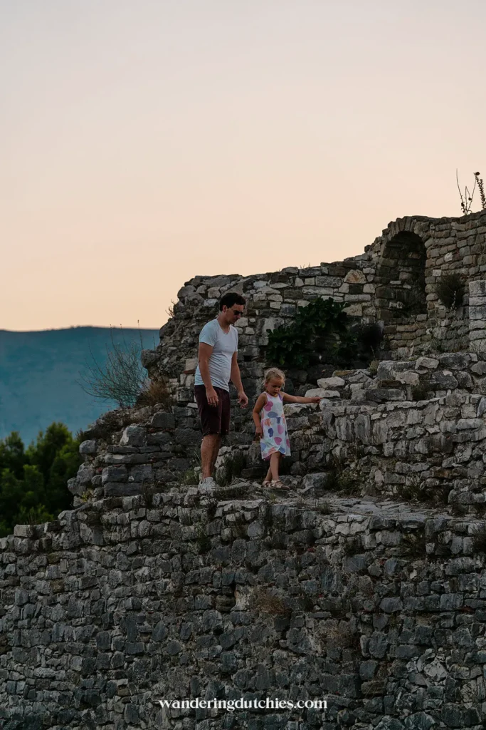 Vader en dochter wandelen over de stenen muren van Berat Castle bij zonsondergang.