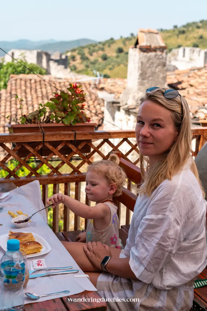 Moeder en kind genieten van traditionele gerechten bij Antipatrea Restaurant in Berat, met uitzicht op de kasteelmuur.