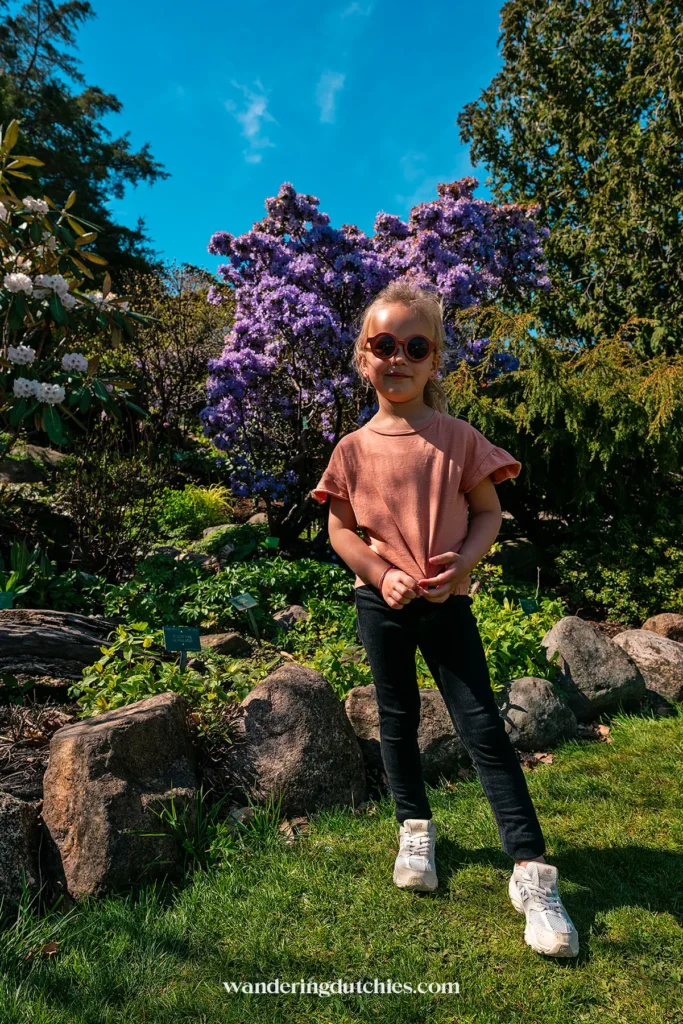 Een jong meisje met zonnebril staat voor een bloeiende paarse struik in Botanisk Have.