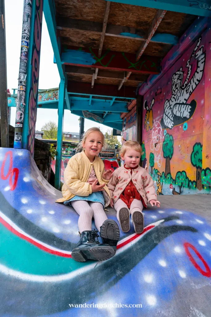 Twee kinderen zitten lachend op een felgekleurde skateramp in Christiana, Kopenhagen.