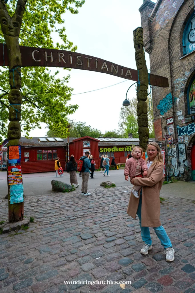Moeder en kind staan onder de iconische houten boog bij de ingang van Christiana, Kopenhagen.