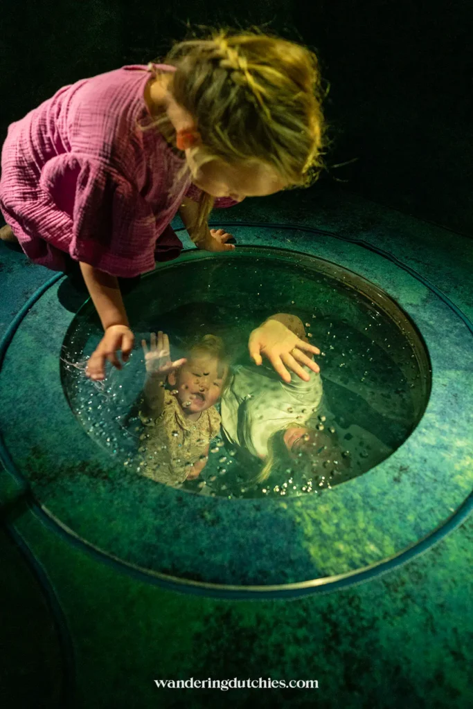 Een nieuwsgierig kind kijkt in een grote, doorzichtige waterbol naar haar moeder en zusje in het Experimentarium.