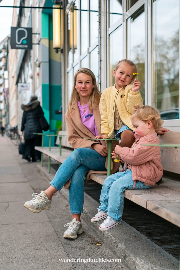 Moeder en dochters zitten ontspannen op een bankje voor een café in Kopenhagen.