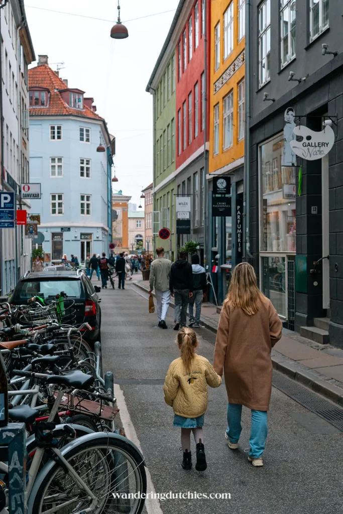 Moeder en dochter wandelen door een kleurrijke straat in Kopenhagen, omringd door fietsen.