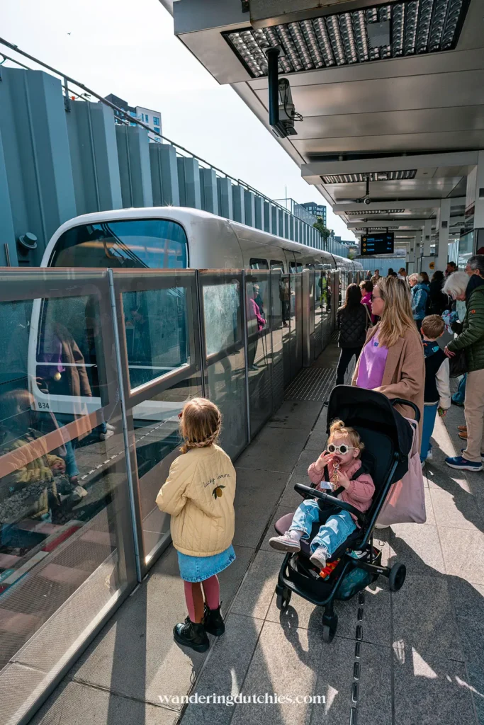 Moeder met kinderwagen en dochter wachten op de metro bij een druk perron in Kopenhagen.