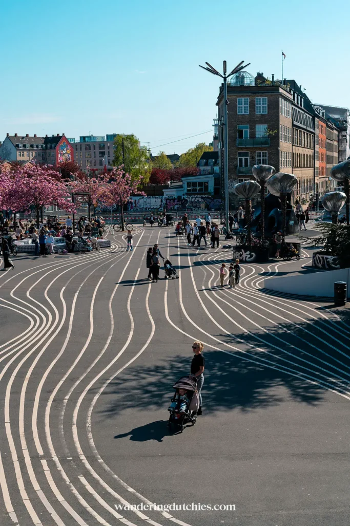 Overzicht van Superkilen Park met bezoekers, roze bloesems en zwart-witte lijnen.