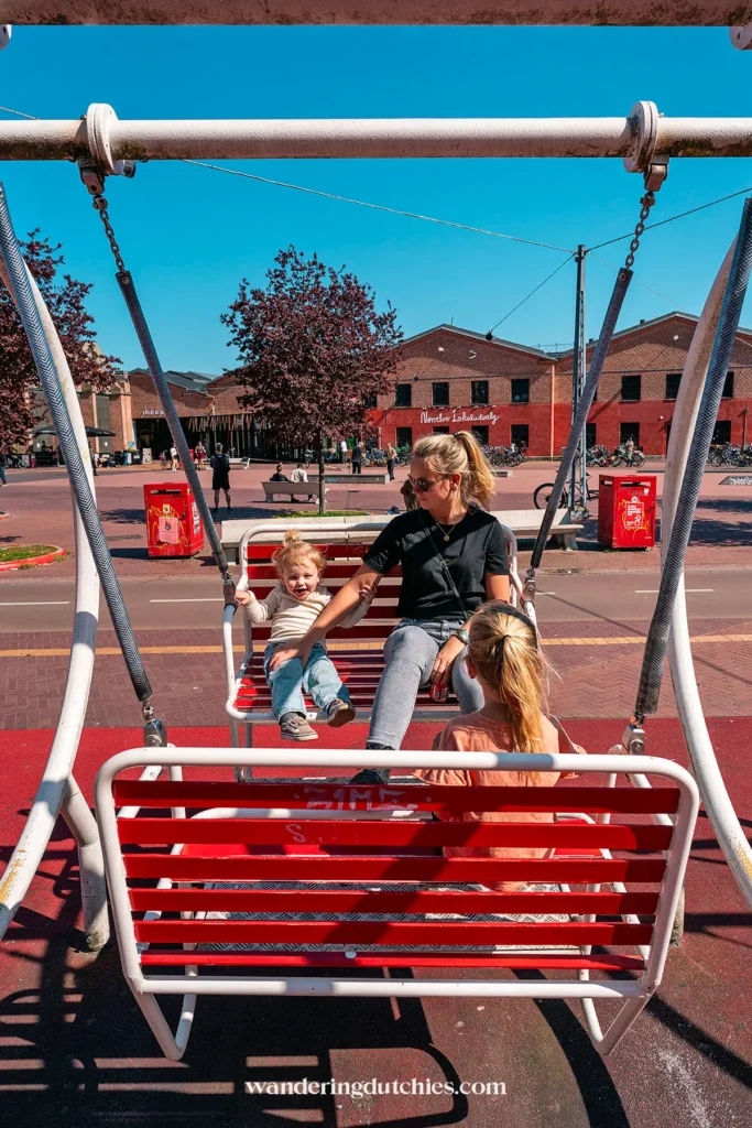 Moeder en kinderen schommelen samen op een grote rode schommel in Superkilen Park, Kopenhagen.