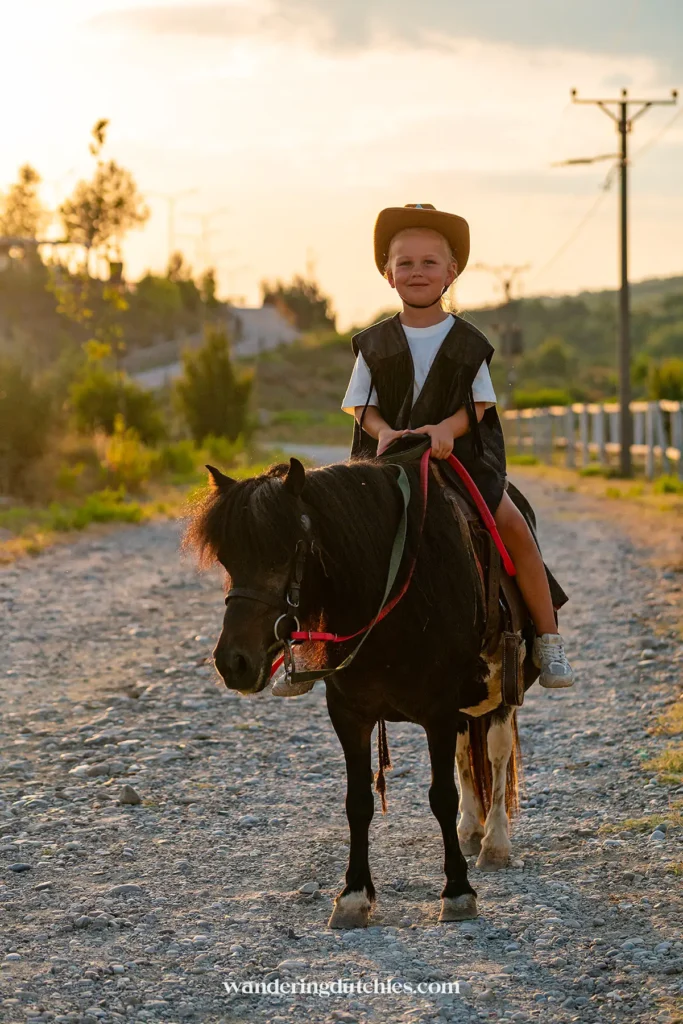 Child enjoying a pony ride at sunset in Albania.