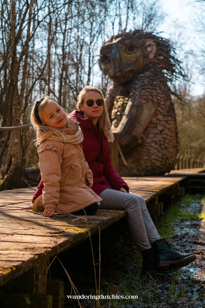 Mother and daughter sitting on the boardwalk near troll Arvid in the Troll Forest of De Schorre.