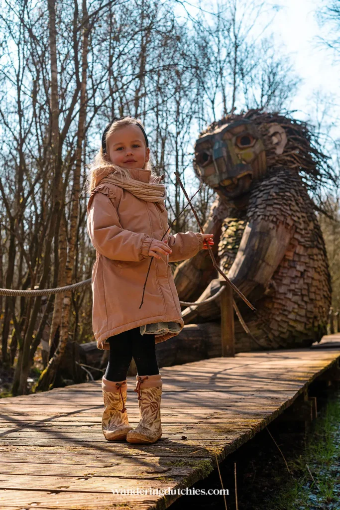 Girl posing on the boardwalk with troll Arvid in the background, Troll Forest of De Schorre.