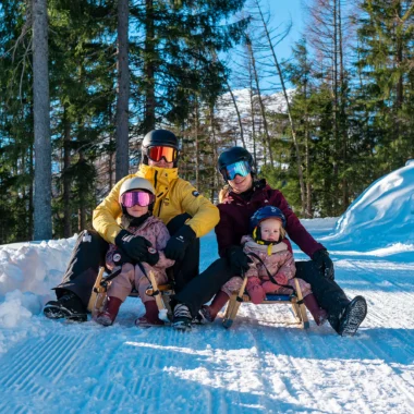 Wintersport in Fügen, Oostenrijk: gezin geniet van een zonnige dag rodelen op een besneeuwde piste in het Zillertal.