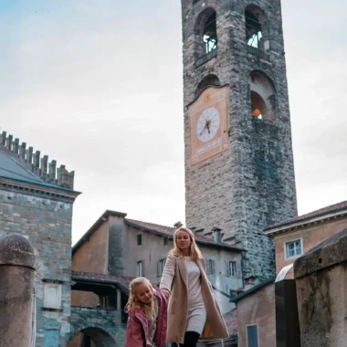Moeder en dochter in Città Alta, Bergamo met de Campanone toren op de achtergrond - een kindvriendelijke stedentrip in Italië.