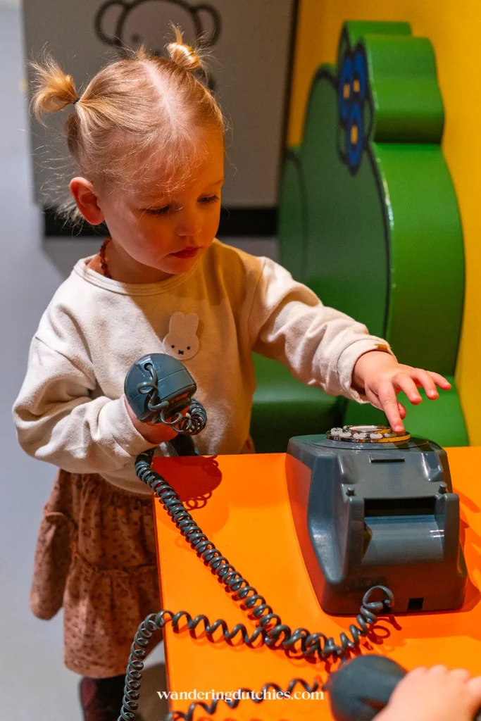 Klein meisje speelt met een ouderwetse telefoon in het nijntje museum in Utrecht.