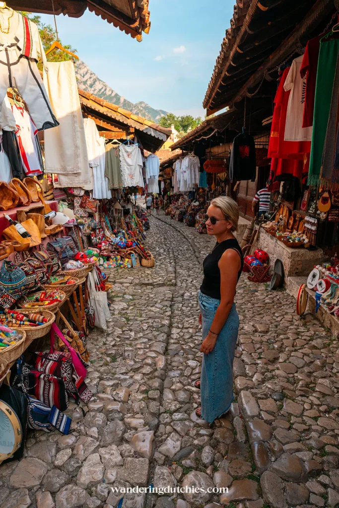 Vrouw loopt door de bazaar van Krujë met uitzicht op de bergen.