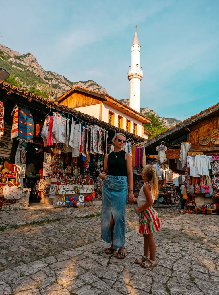 Vrouw en kind in de bazaar van Krujë met uitzicht op minaret.
