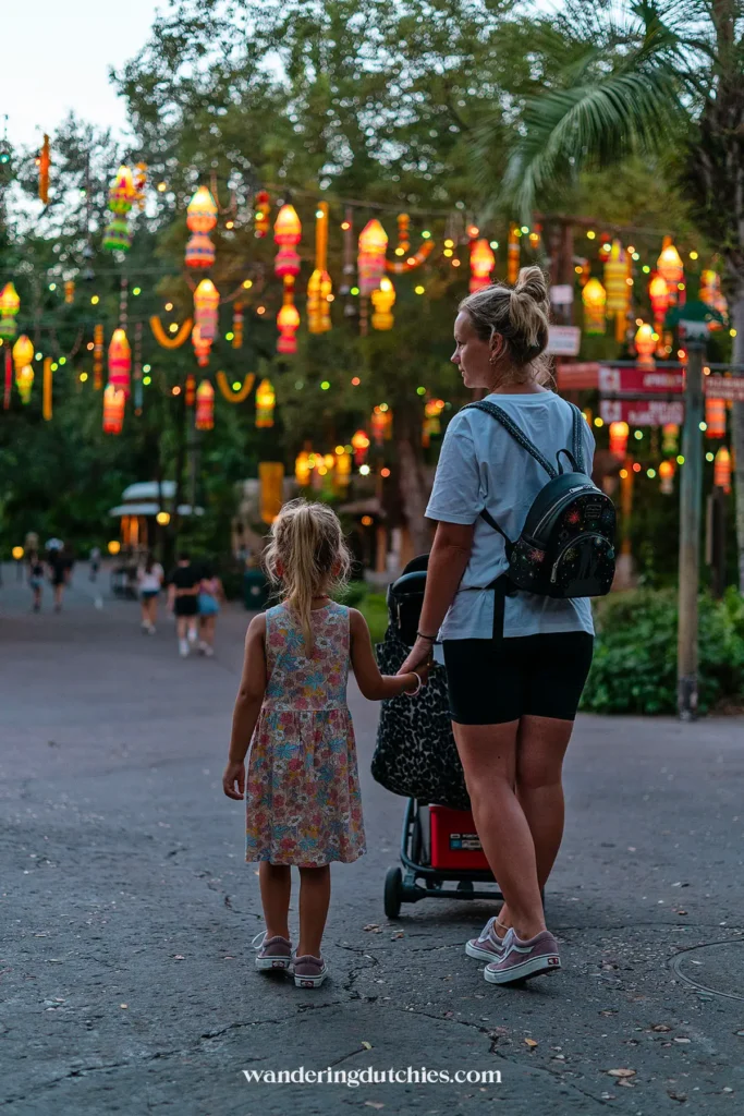 Moeder en dochter wandelen onder kleurrijk verlichte lantaarns in het park tijdens de schemering.