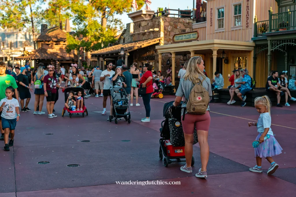 Moeder met twee jonge kinderen wandelt door Frontierland in Magic Kingdom, Disney World, op een zonnige dag met een buggy en rugzak.