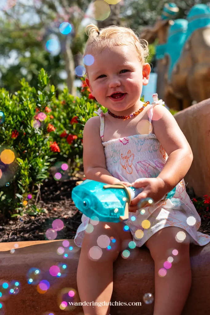 Dreumes speelt met bellenblaas bij Magic Kingdom in Walt Disney World, gekleed in een Disney-jurkje, met kleurrijke bellen op de voorgrond.
