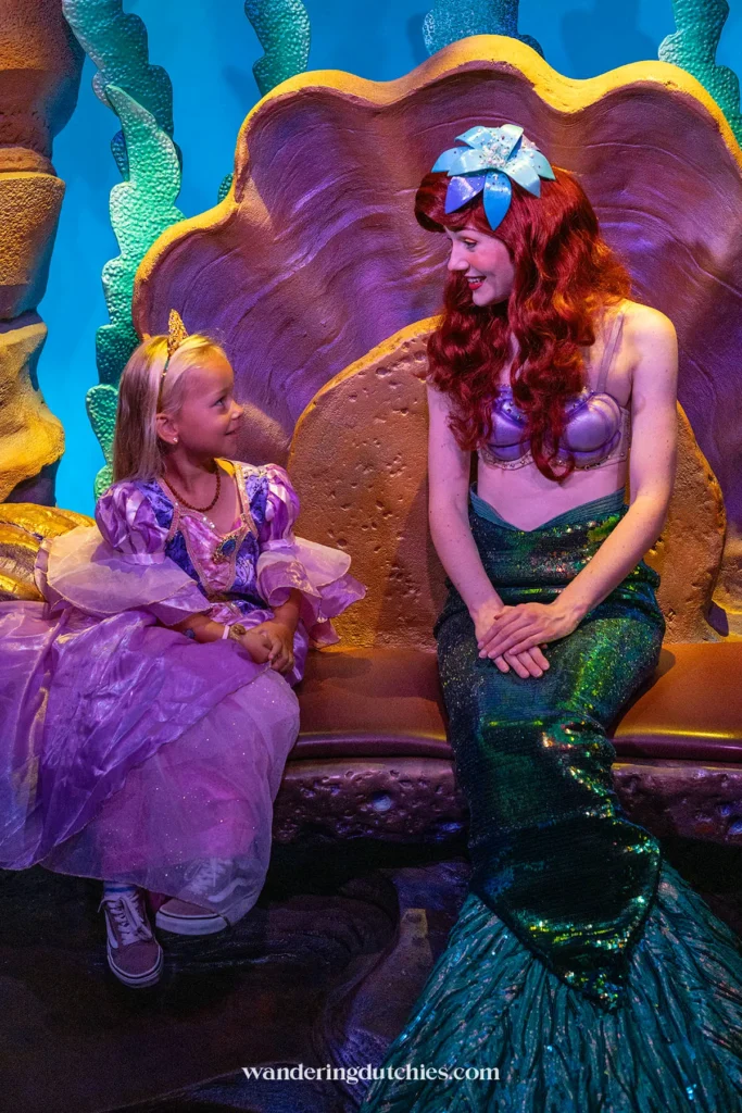 Klein meisje in paarse jurk praat met Ariel tijdens een ontmoeting in Walt Disney World.