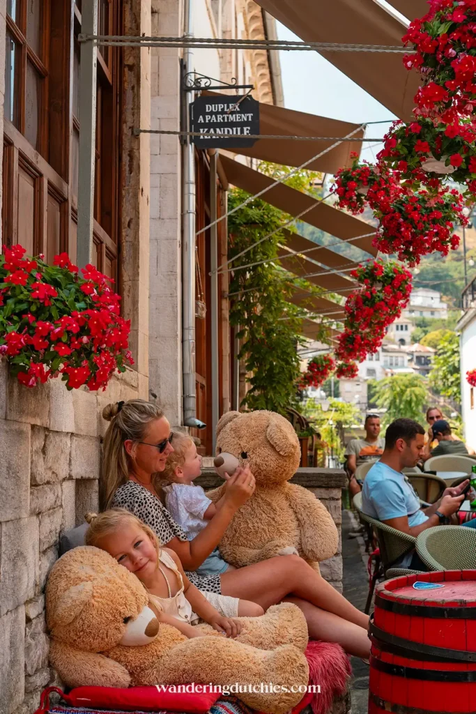 Moeder en kinderen spelen met grote knuffelberen op een terras in de bazaar van Gjirokaster