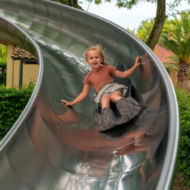 Meisje glijdt lachend van een metalen glijbaan in een speeltuin