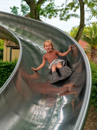 Meisje glijdt lachend van een metalen glijbaan in een speeltuin