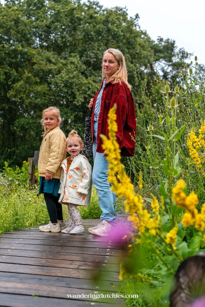 Moeder met twee jonge kinderen op houten pad in de tuin van Boscafé de Busjop in Heythuysen, omringd door bloemen