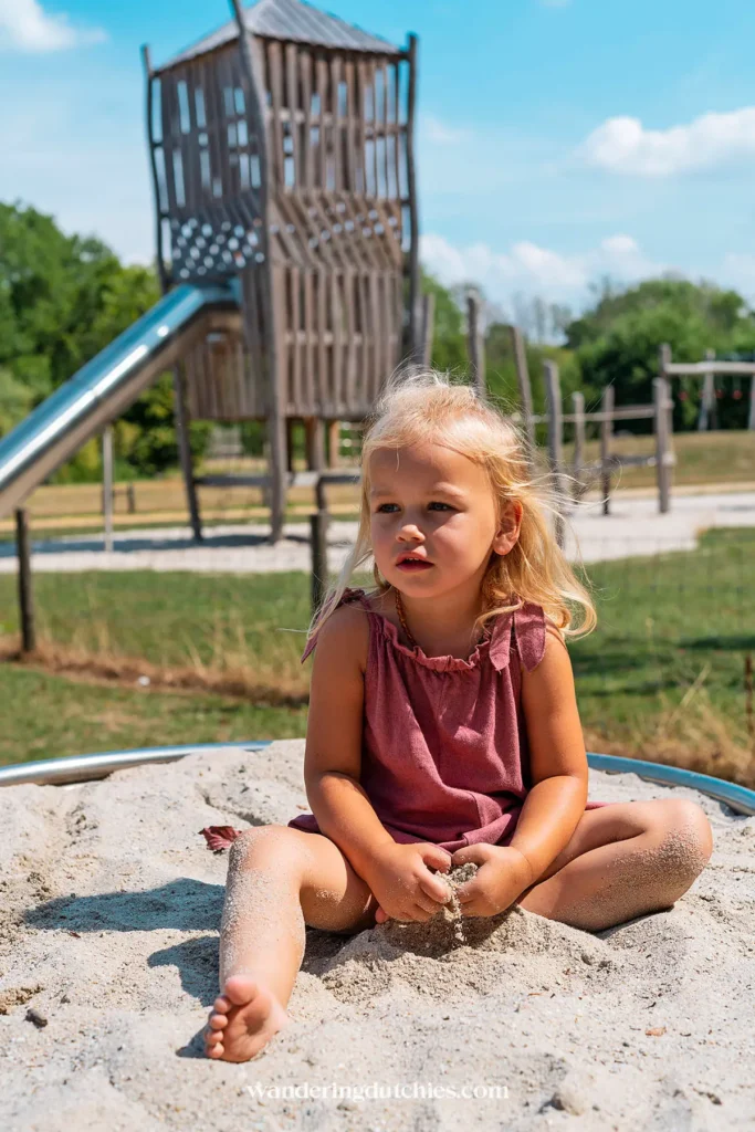 Meisje speelt in de zandbak bij de speeltuin van Kanjel in Maastricht met houten klimtoestellen op de achtergrond