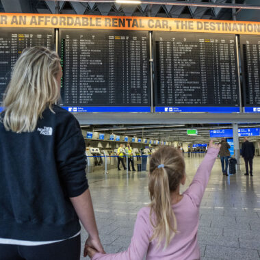 Moeder en dochter bij het vluchtoverzicht op Frankfurt Airport, klaar om te vliegen vanaf Frankfurt