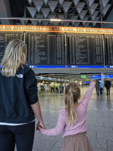 Moeder en dochter bij het vluchtoverzicht op Frankfurt Airport, klaar om te vliegen vanaf Frankfurt