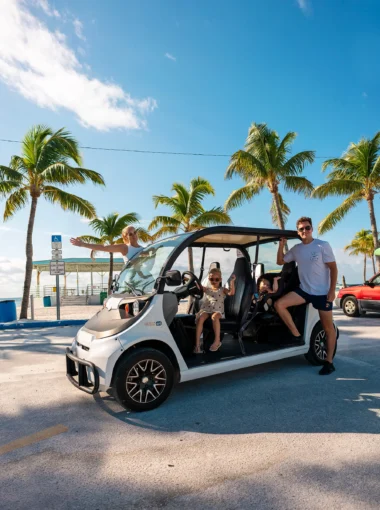 Gezin op roadtrip door Florida in elektrische golfkar in Key West met palmbomen op de achtergrond
