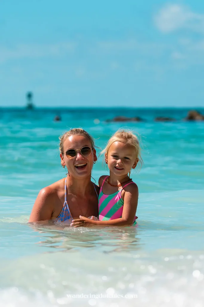 Moeder en dochter lachen in helder turquoise zeewater bij een ondiep strand in de Florida Keys.