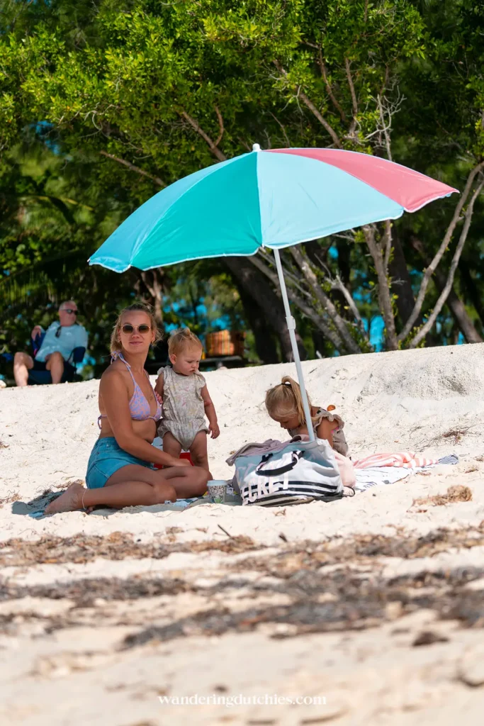 Moeder met twee kinderen onder een mint en roze parasol op het zandstrand in de Florida Keys.