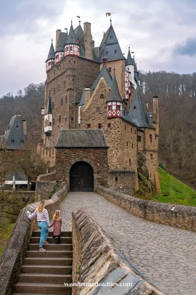 Mother and daughter walking hand in hand across the castle bridge of Burg Eltz.