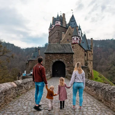 Gezin wandelt over de brug naar Burg Eltz, een sprookjesachtig kasteel in Duitsland, populair uitje in de Moezelregio.