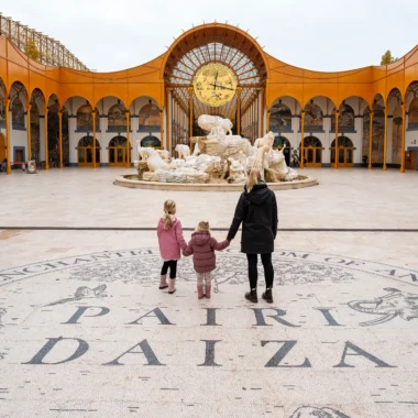 Moeder en haar dochters bij de indrukwekkende ingang van Pairi Daiza met kinderen, met de gouden klok en fontein op de achtergrond.