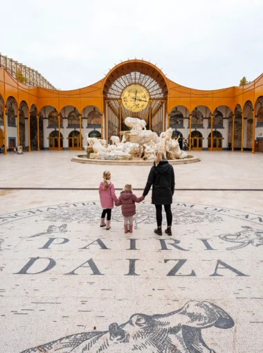 Moeder en haar dochters bij de indrukwekkende ingang van Pairi Daiza met kinderen, met de gouden klok en fontein op de achtergrond.