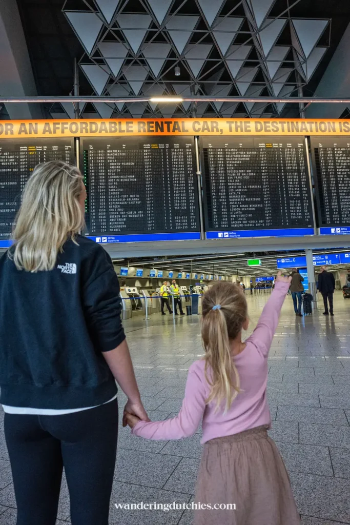 Moeder en dochter bekijken vertrekborden op Frankfurt Airport.
