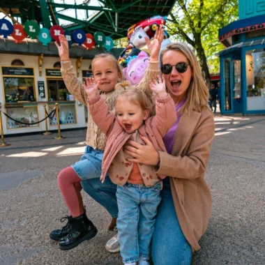 Gezin met twee jonge kinderen dat lachend poseert bij de ingang van Tivoli Gardens in Kopenhagen.
