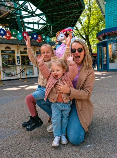 Gezin met twee jonge kinderen dat lachend poseert bij de ingang van Tivoli Gardens in Kopenhagen.