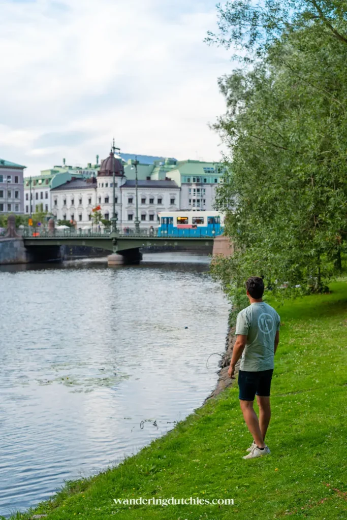 Man wandelt langs het water in het centrum van Göteborg met uitzicht op een brug en blauwe tram.