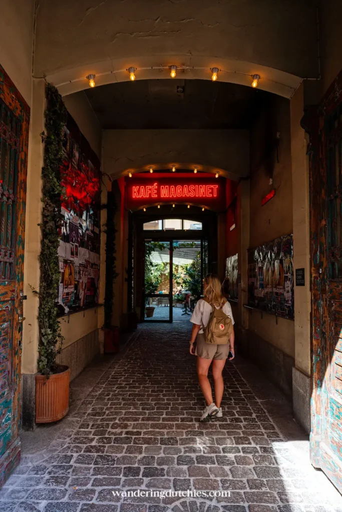 Vrouw loopt de sfeervolle ingang van Kafé Magasinet in Göteborg binnen, met rode neonletters boven de deur.