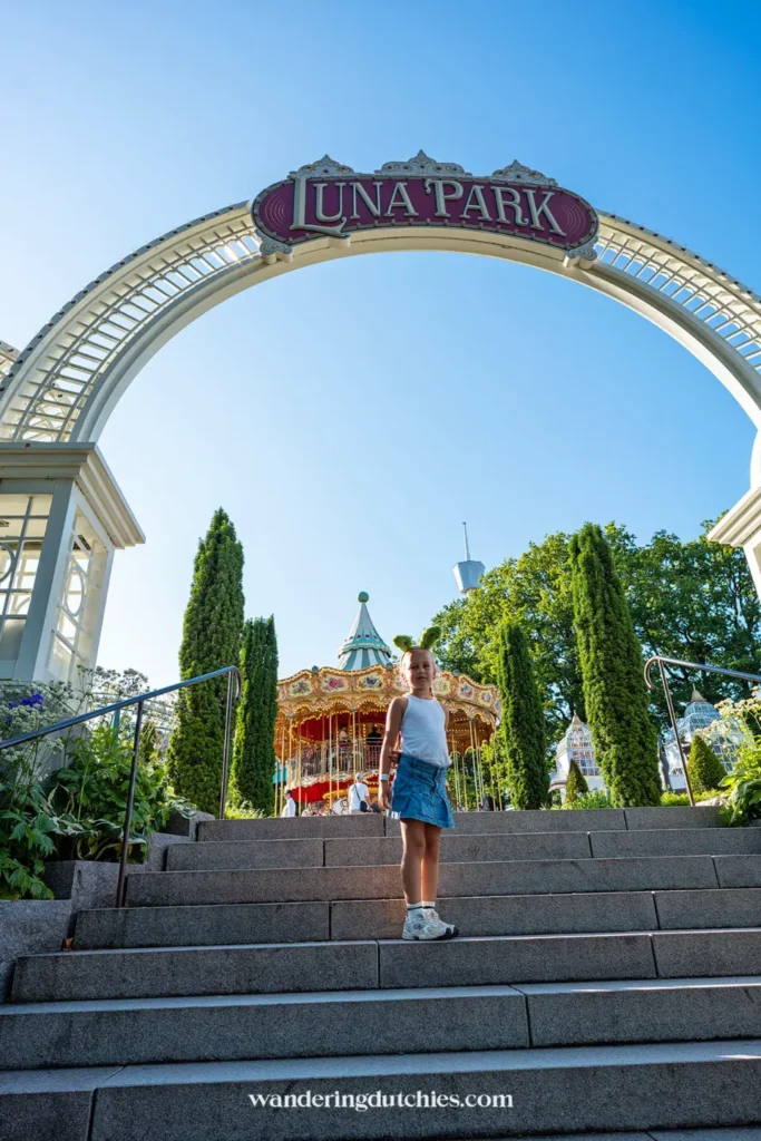 Meisje loopt onder de boog van Luna Park in Liseberg met de draaimolen op de achtergrond.